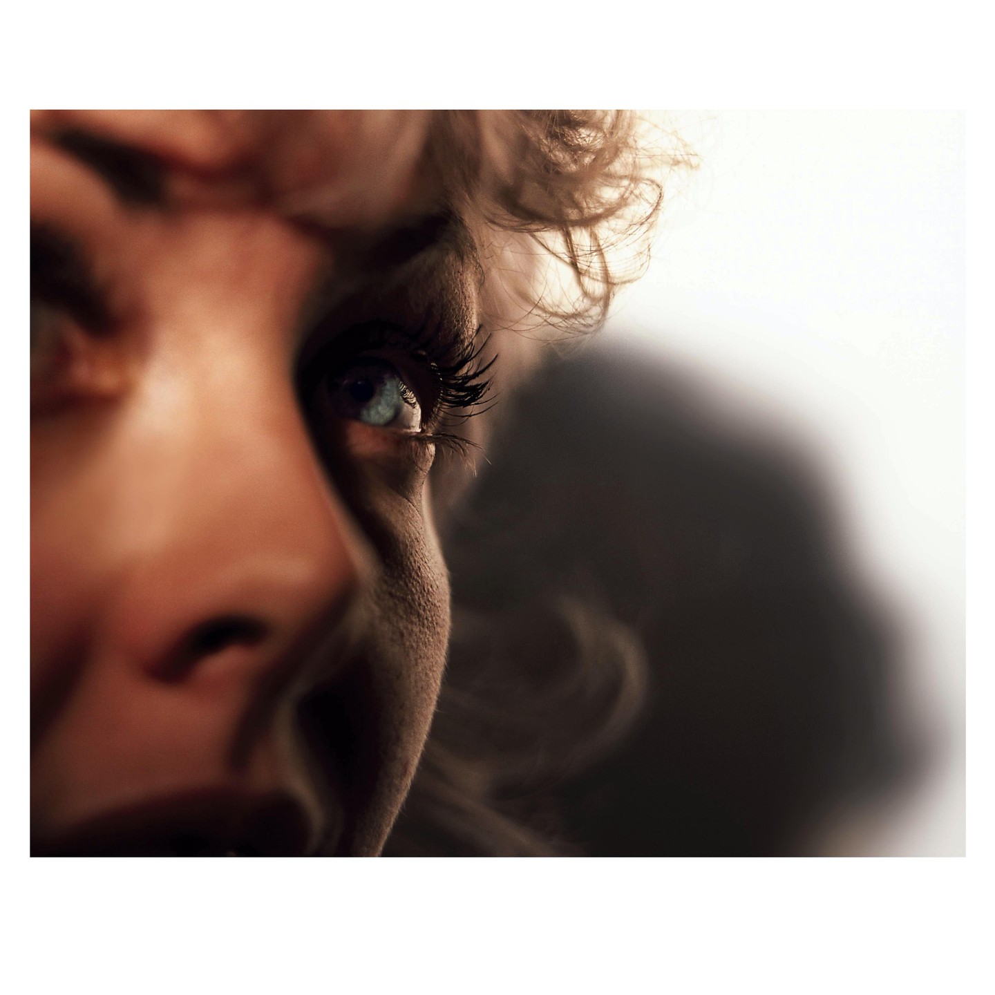 A close-up portrait shows a woman's eye with long eyelashes and curly hair.