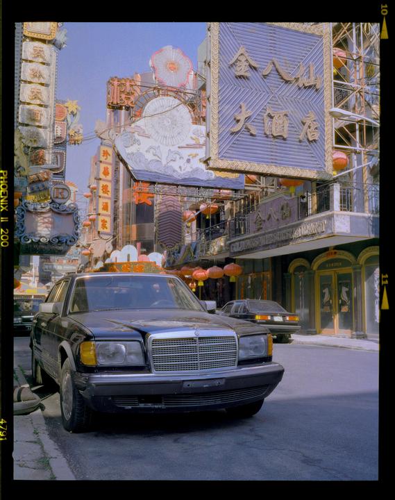 A black car is parked on a street lined with buildings adorned with ornate signs and red lanterns.