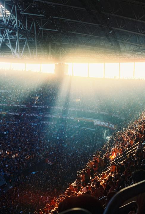 Sunlight streams into a stadium filled with a large crowd of people.
