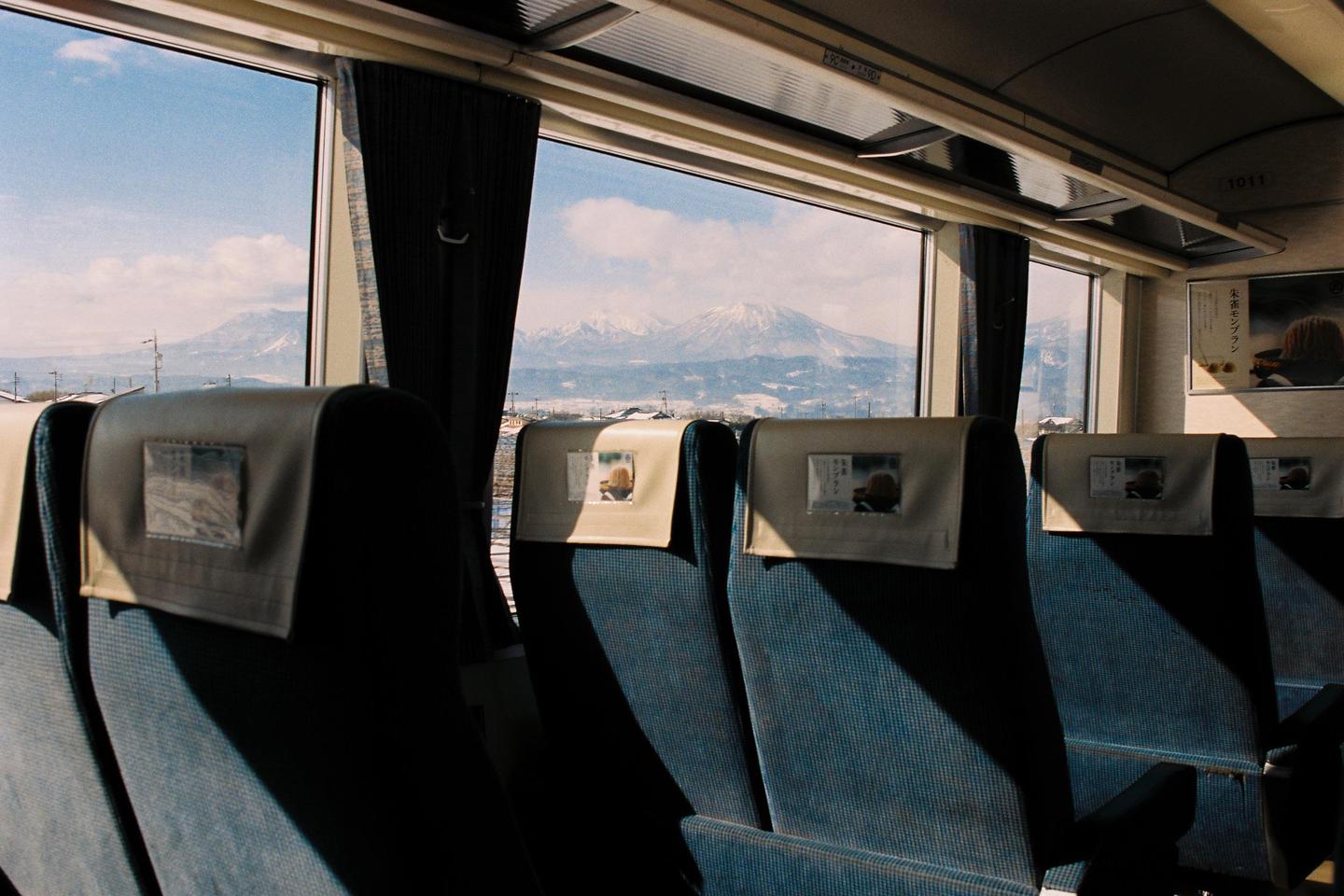 The interior of a train car with blue seats and a view of snow-capped mountains through the window.