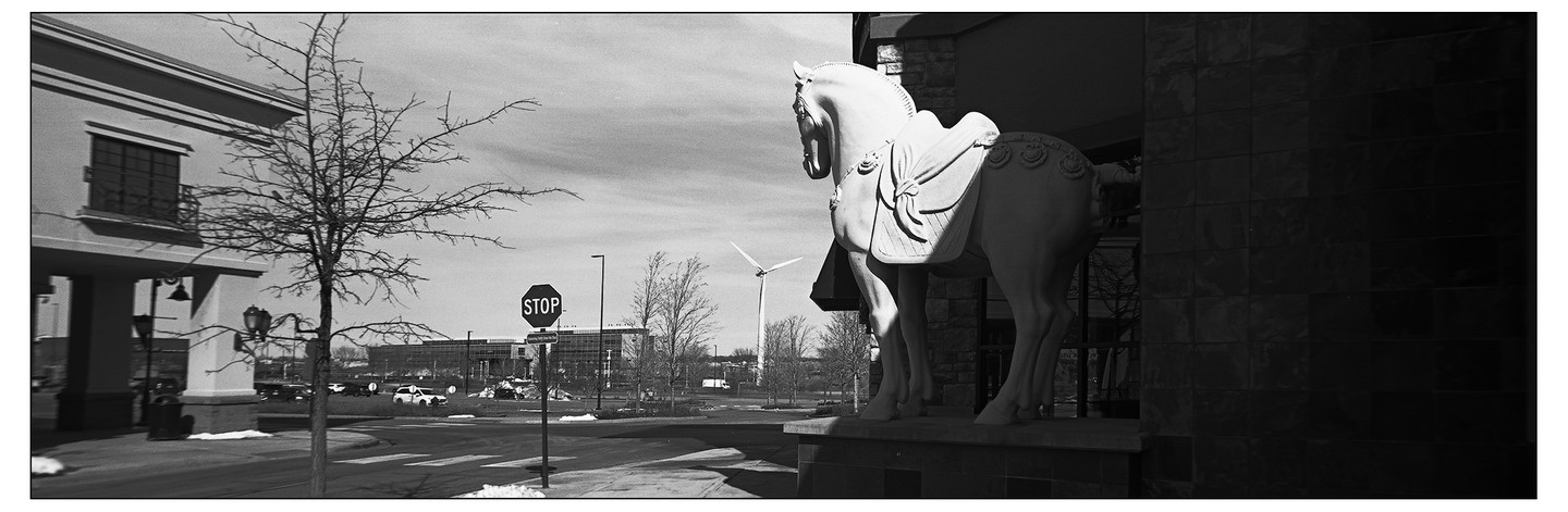 A statue of a horse stands next to a building with a stop sign and a wind turbine in the background.