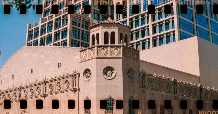 An ornate building with a tower and a modern building with blue windows are visible against a clear sky.