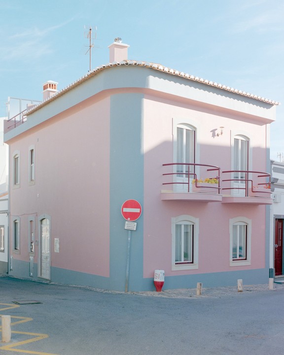 A pastel pink building with blue trim stands on a street corner under a clear sky.