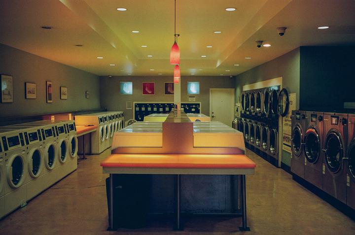 A long, empty laundromat is lit by warm, colorful lights.
