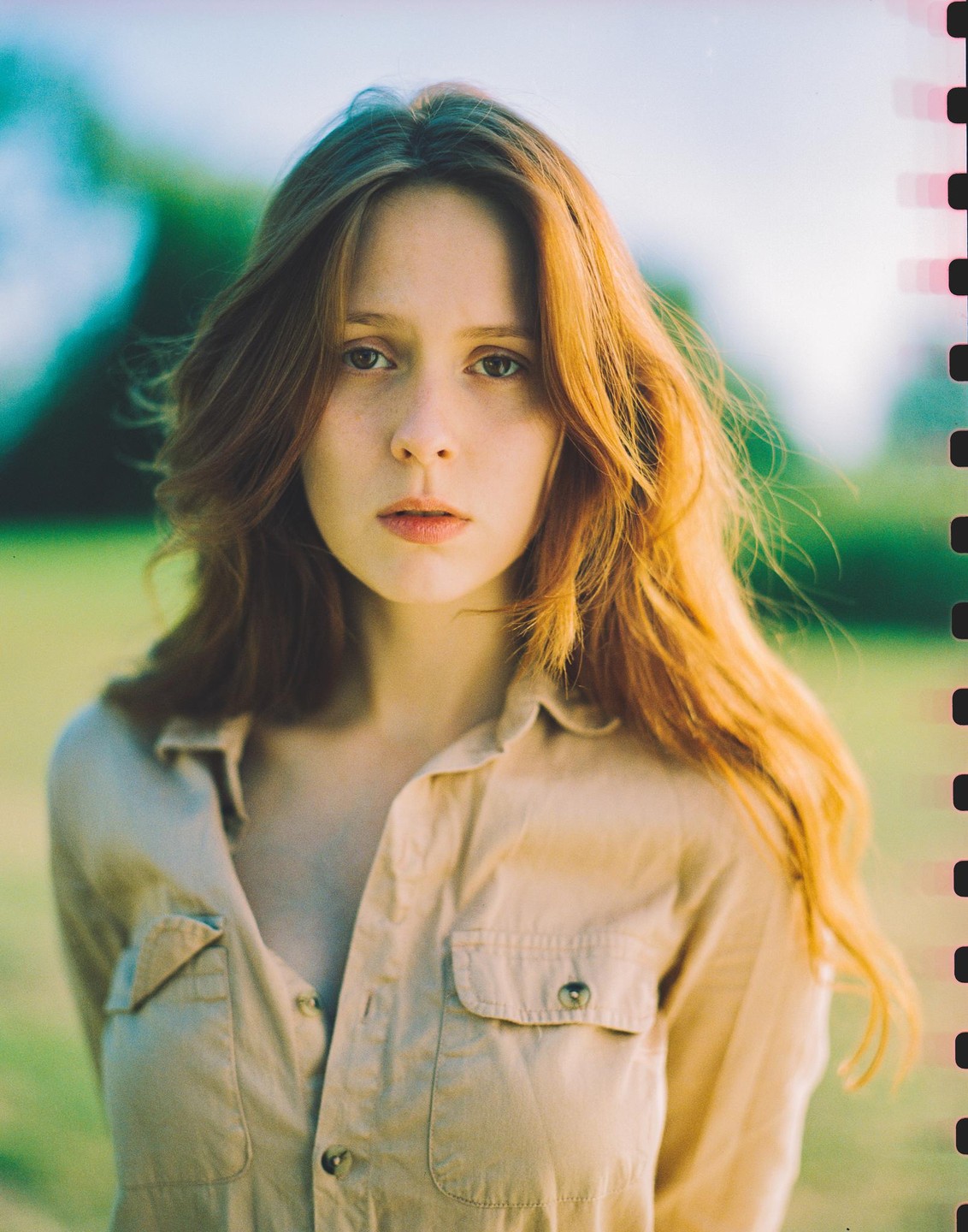 A woman with long red hair wears a tan shirt in a portrait.