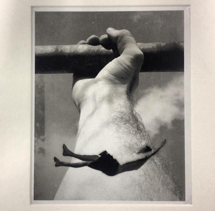 A large hand holds onto a bar while a small figure falls through the air below.