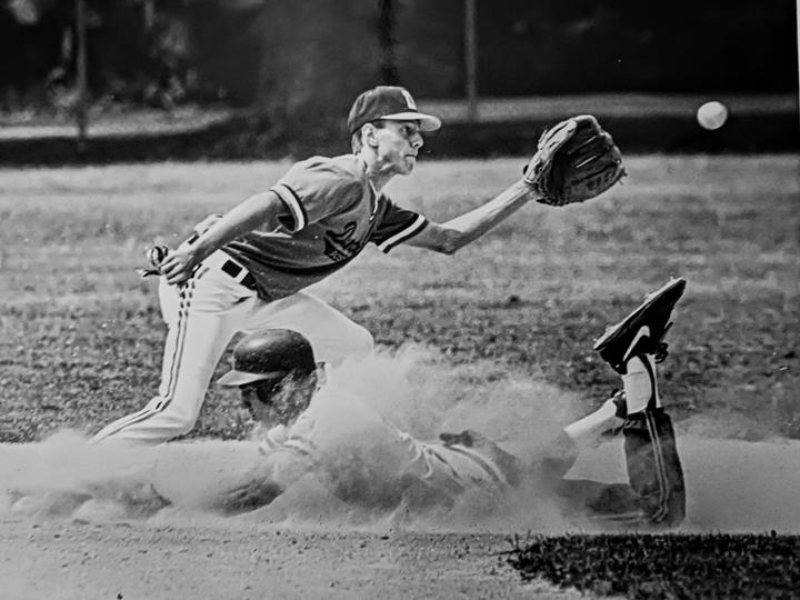 A baseball player slides into second base as another player reaches for a ball.