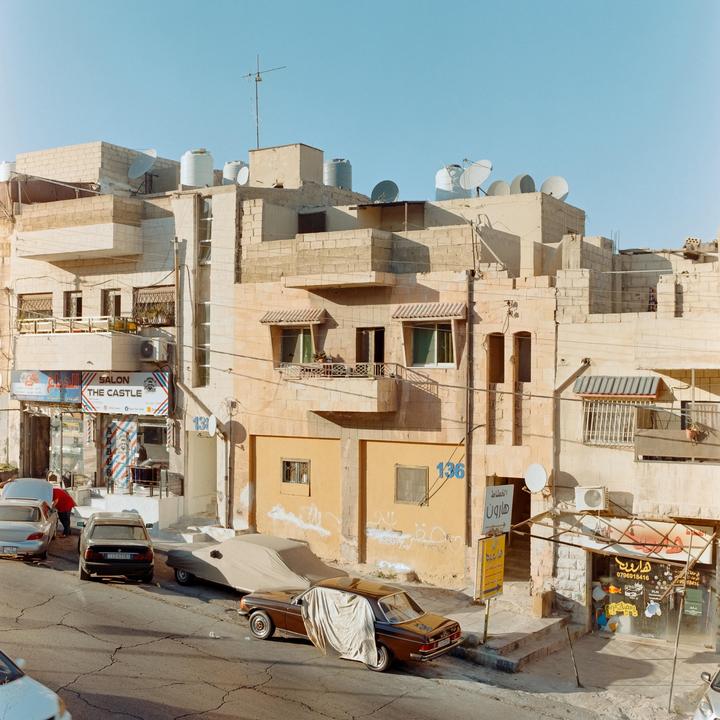 A street in Jordan is lined with buildings and cars, with a barber shop visible on the left.