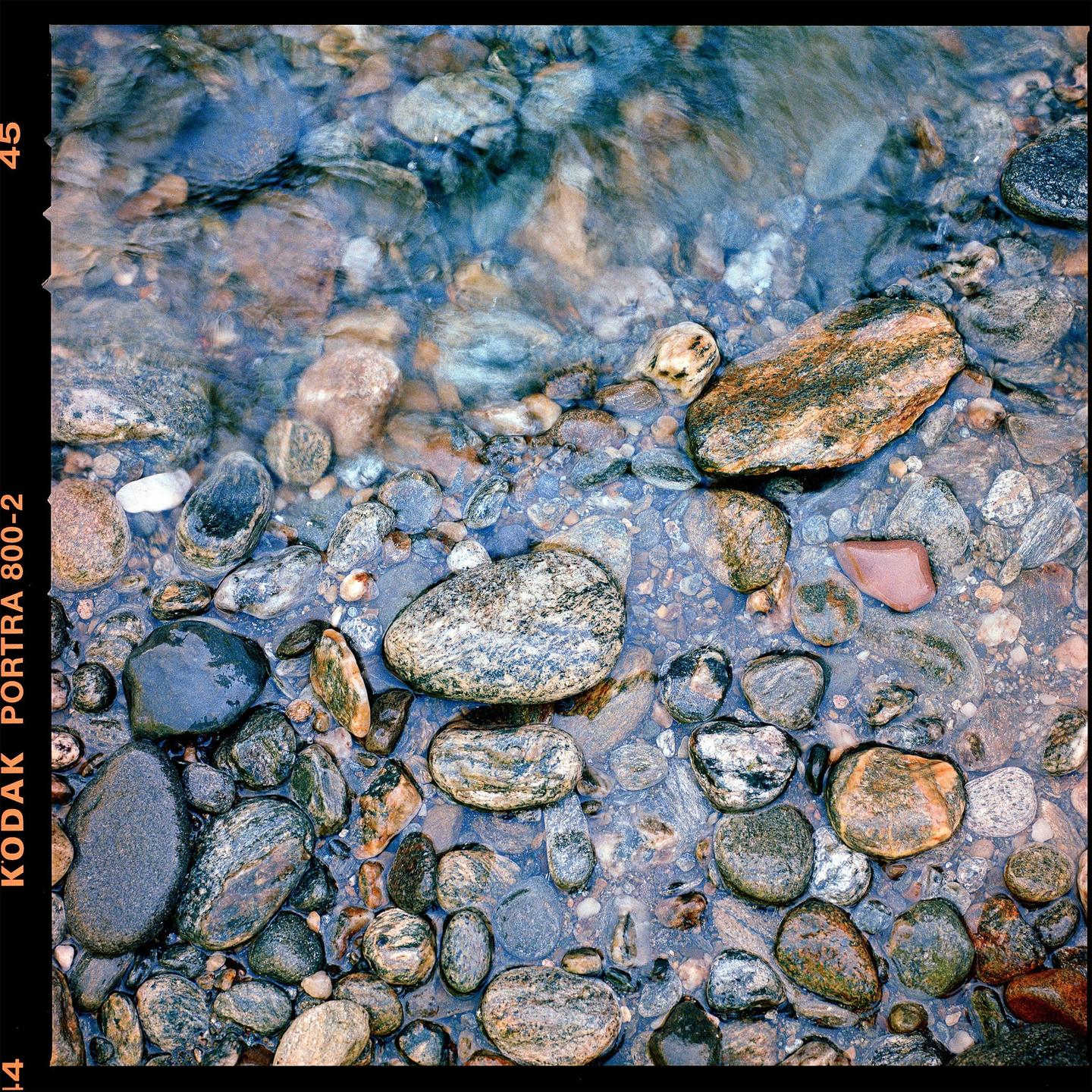 A collection of smooth, colorful stones are visible through clear, shallow water.