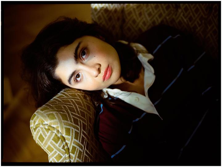 A woman with dark hair and a striped shirt rests her head on a patterned armchair.
