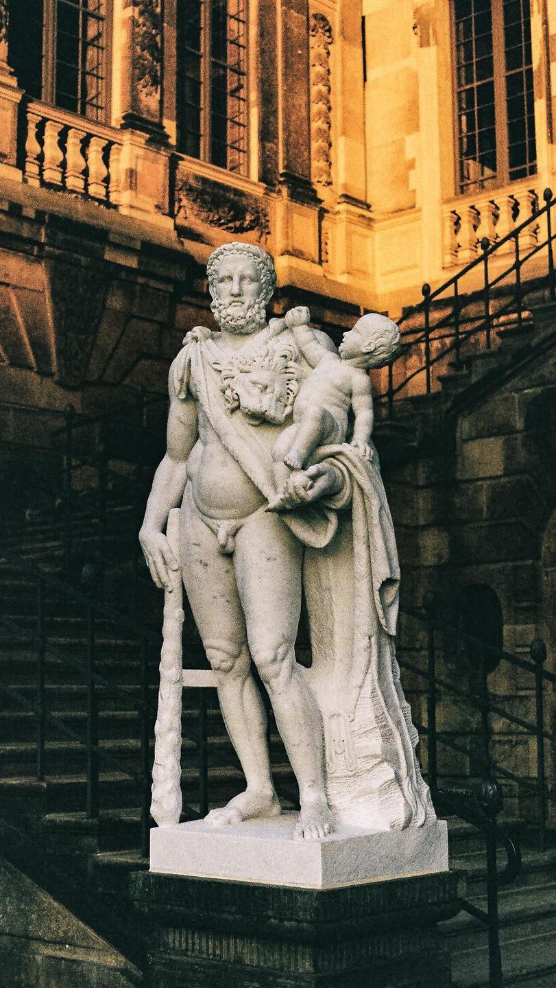 A statue of a man holding a child stands in front of a building with windows and railings.