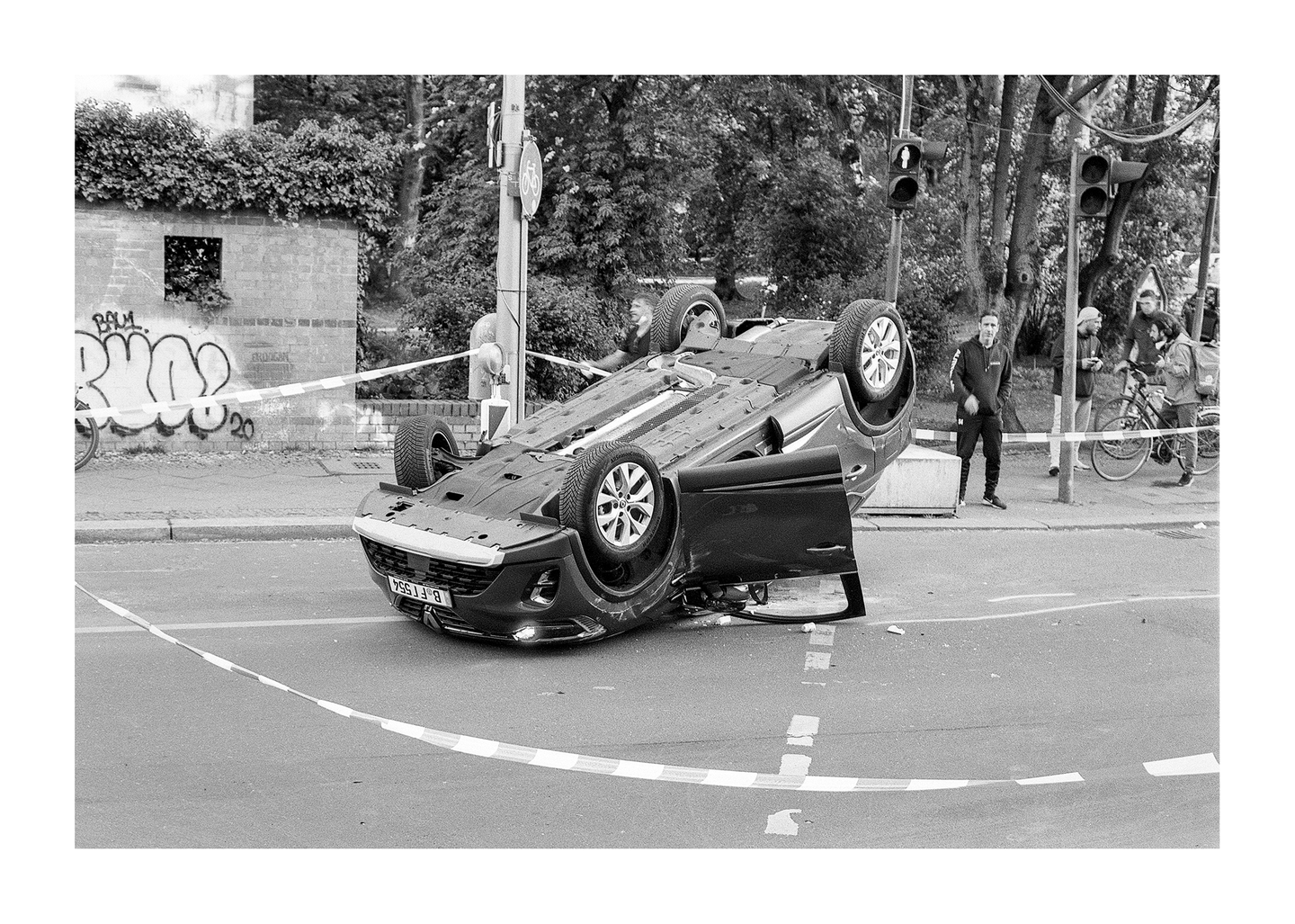 A car is overturned in the middle of a street with people standing nearby.