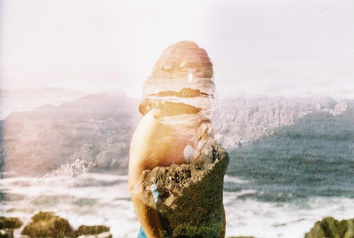 A double exposure shows a woman's profile overlaid with a rocky coastline and mountains.