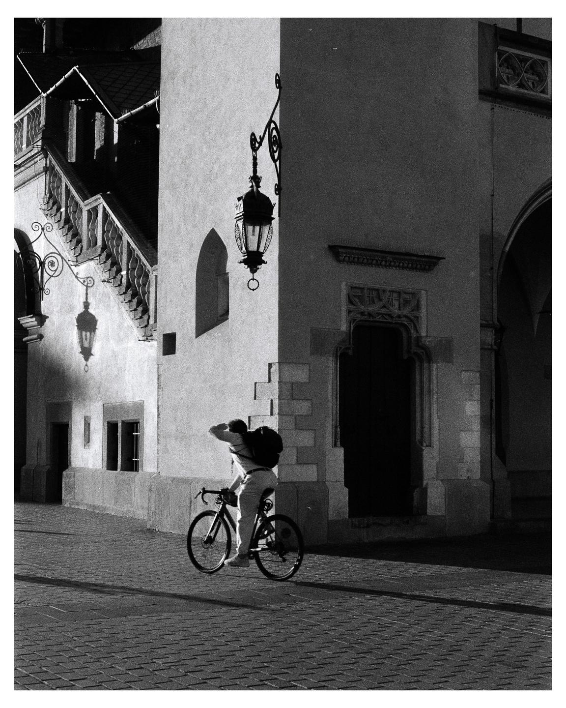 A man on a bicycle is riding past a building with ornate lanterns and a staircase.