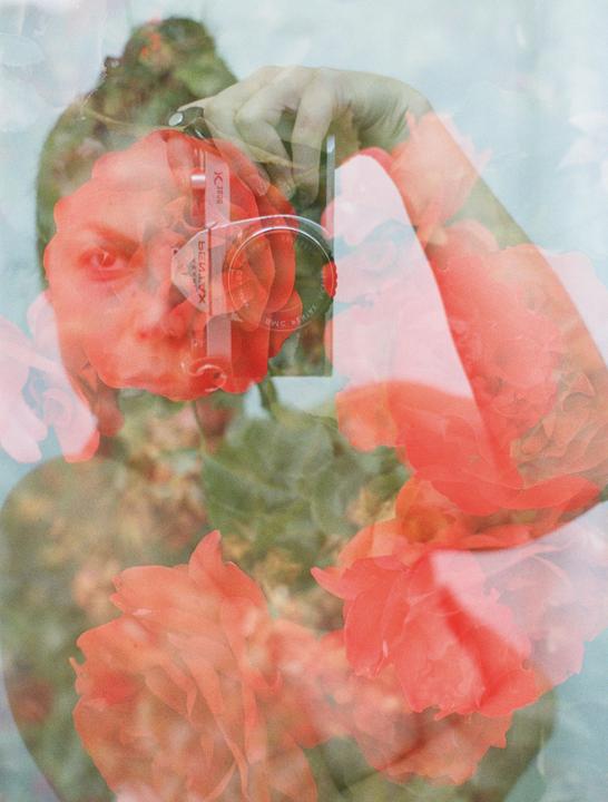 A woman's face is visible through a double exposure with red roses and a reflection of a camera.