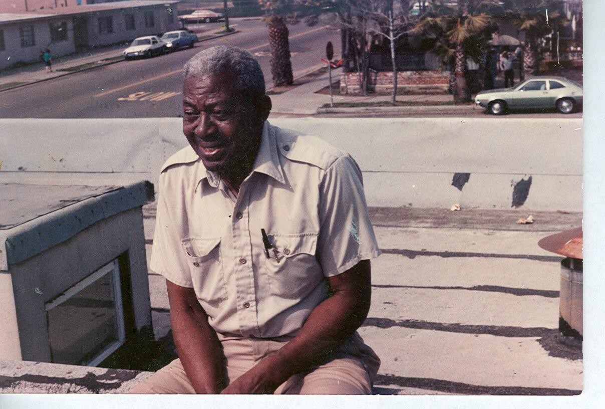 A man sits on a rooftop with a street and buildings in the background.