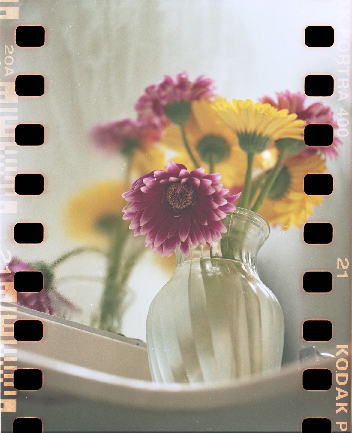 A bouquet of pink and yellow gerbera daisies sits in a clear glass vase on a white surface.