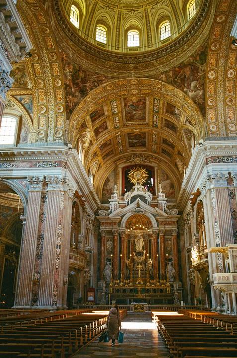A woman walks down the aisle of a grand cathedral with ornate golden ceilings and a large altar.