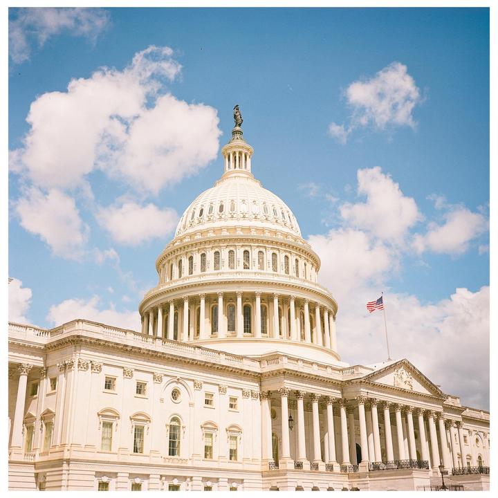 The United States Capitol Building is visible under a blue sky with white clouds.
