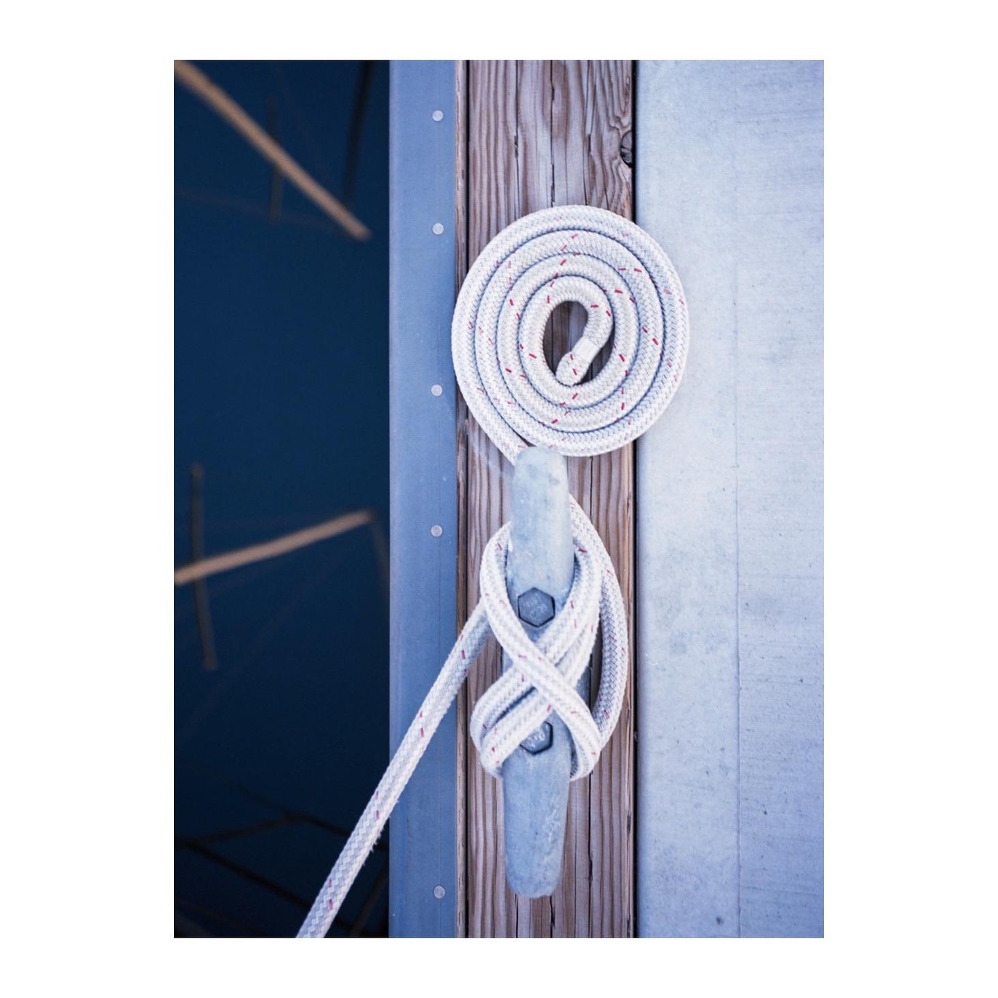 A white rope is coiled around a cleat on a wooden dock next to blue water.