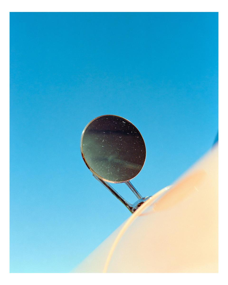 A side mirror of a vehicle is visible against a clear blue sky.