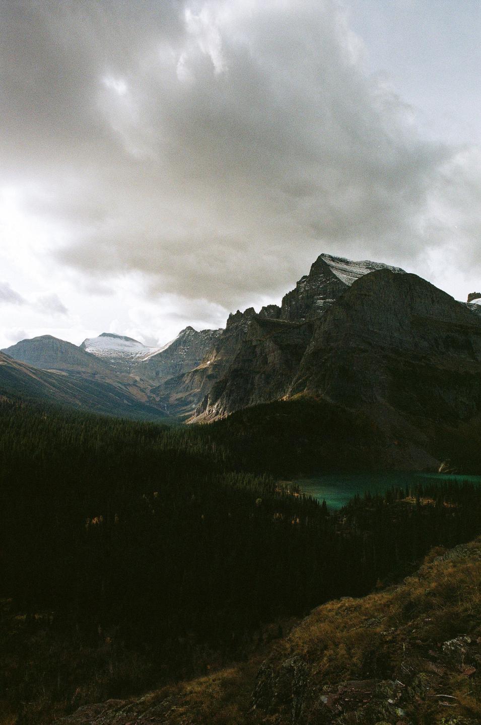A mountain range with a forest and a lake is visible under a cloudy sky.