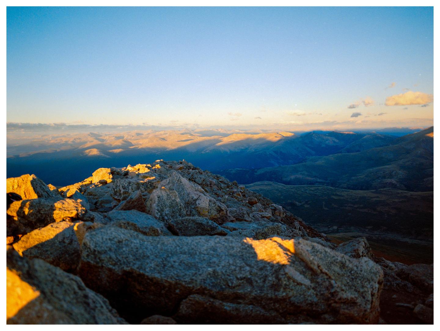 The sun illuminates the rocky peak of a mountain overlooking a valley.