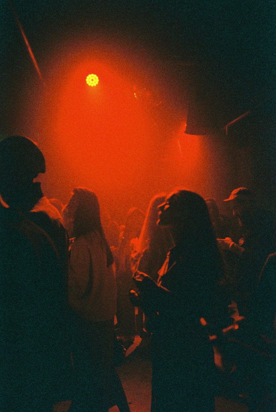 A crowd of people are silhouetted in a dark bar with a bright red light.