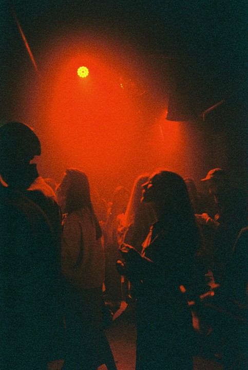 A crowd of people are silhouetted in a dark bar with a bright red light.