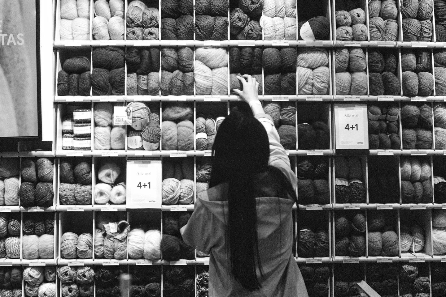 A woman reaches for a skein of yarn from a large display of yarn in a store.