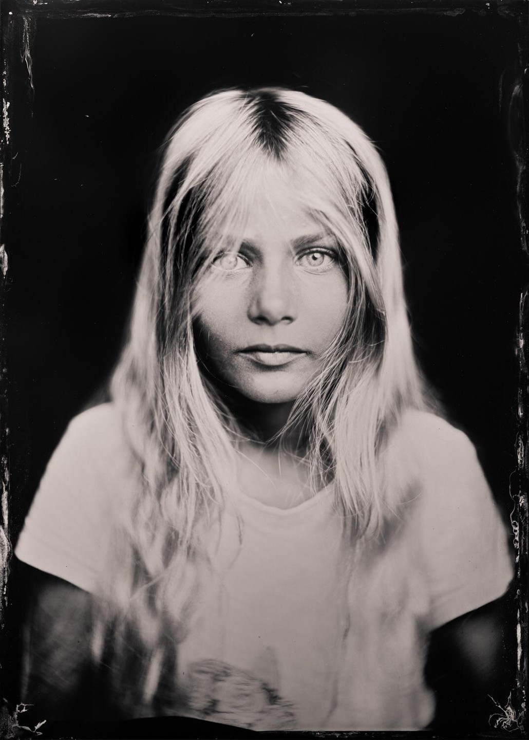 A young girl with long, light hair looks directly at the viewer.
