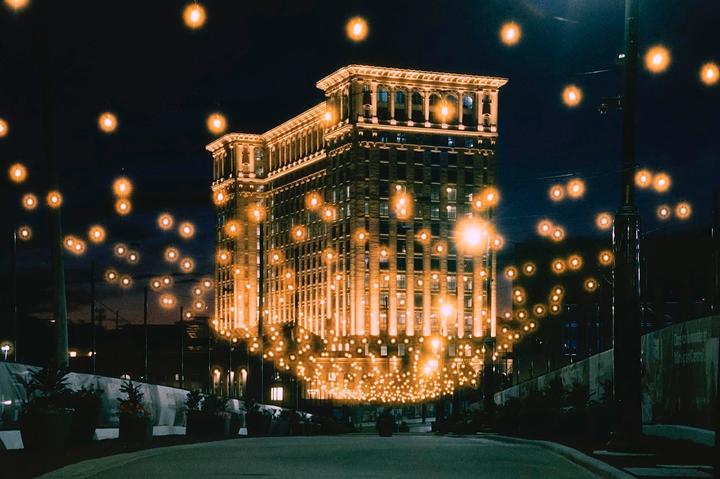 A large building is illuminated at night with many glowing lights in the foreground and background.