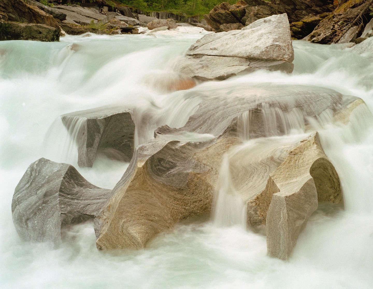 Water flows over and around large rocks in a river.