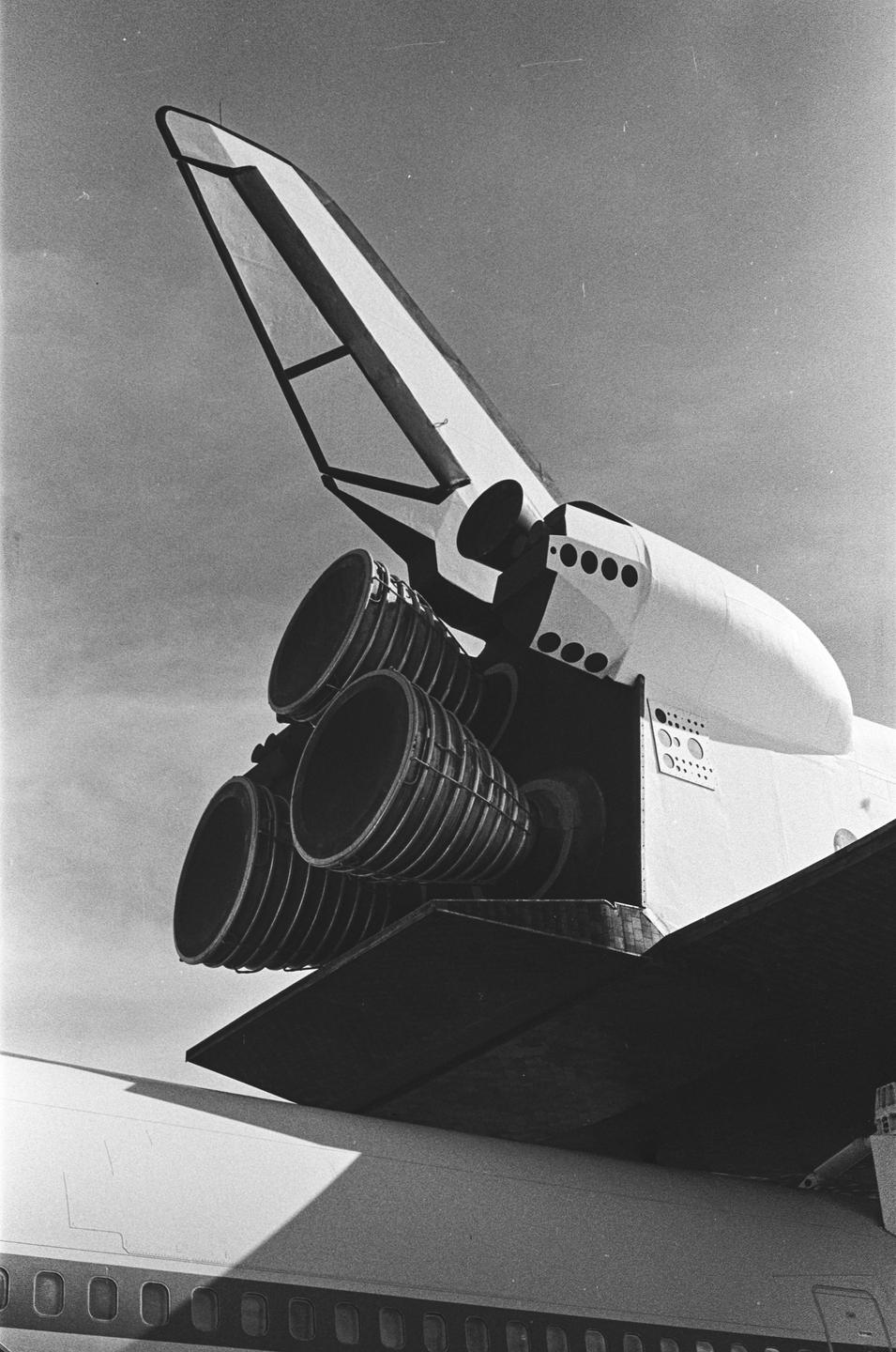 A space shuttle is mounted on top of an airplane, with its tail and engines prominently visible.