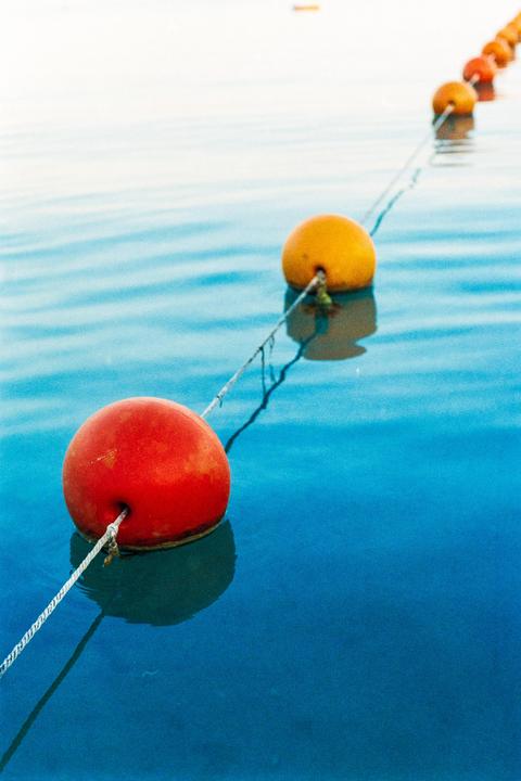 A line of red and orange buoys floats on blue water.