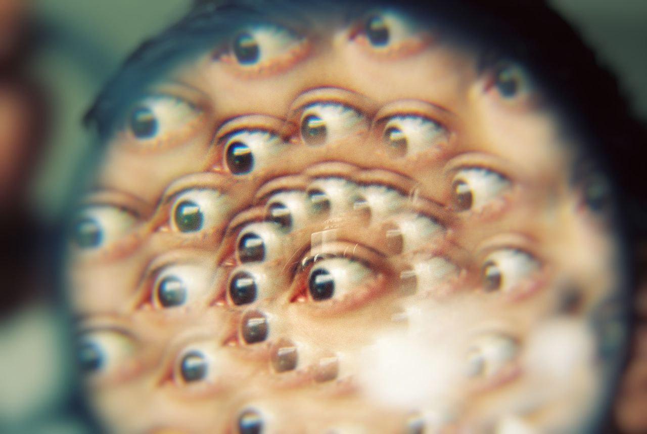 A person's face is distorted into many eyes looking in different directions.