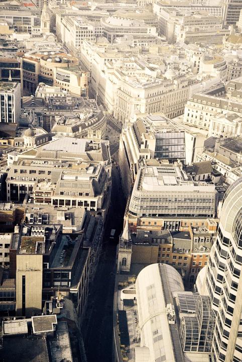 An aerial view shows a dense urban landscape with many buildings and a narrow street.