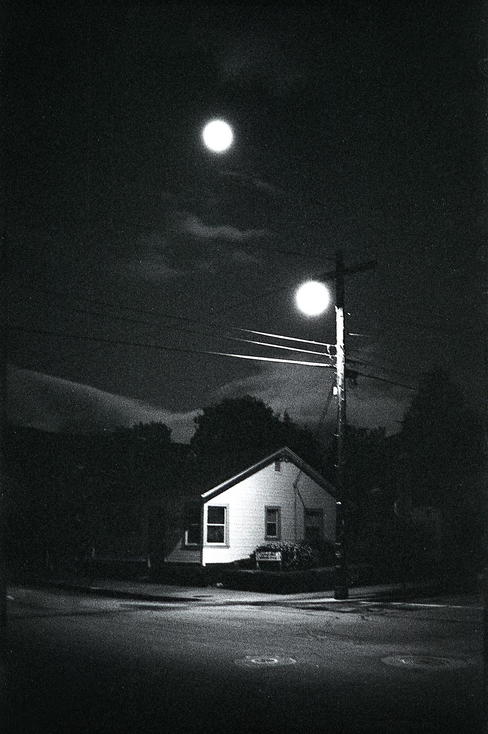 A small house is illuminated by a street light and a bright orb in the night sky.