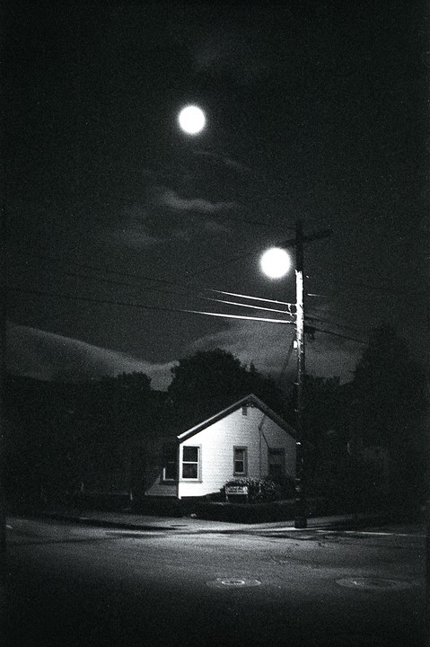 A small house is illuminated by a street light and a bright orb in the night sky.