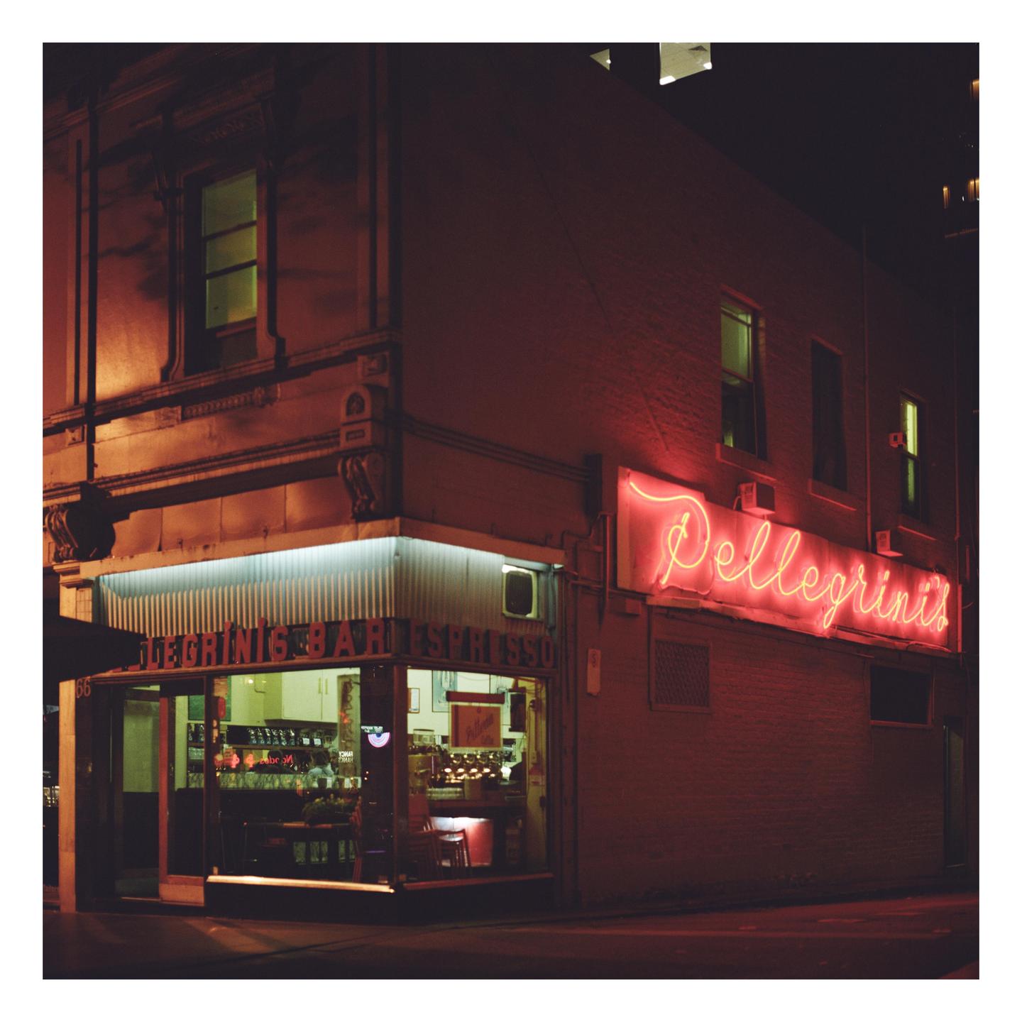 A neon sign for Pellegrini's Bar Espresso illuminates the corner of a building at night.