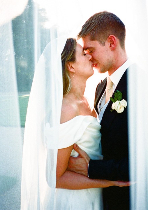 A bride and groom kiss under a veil.