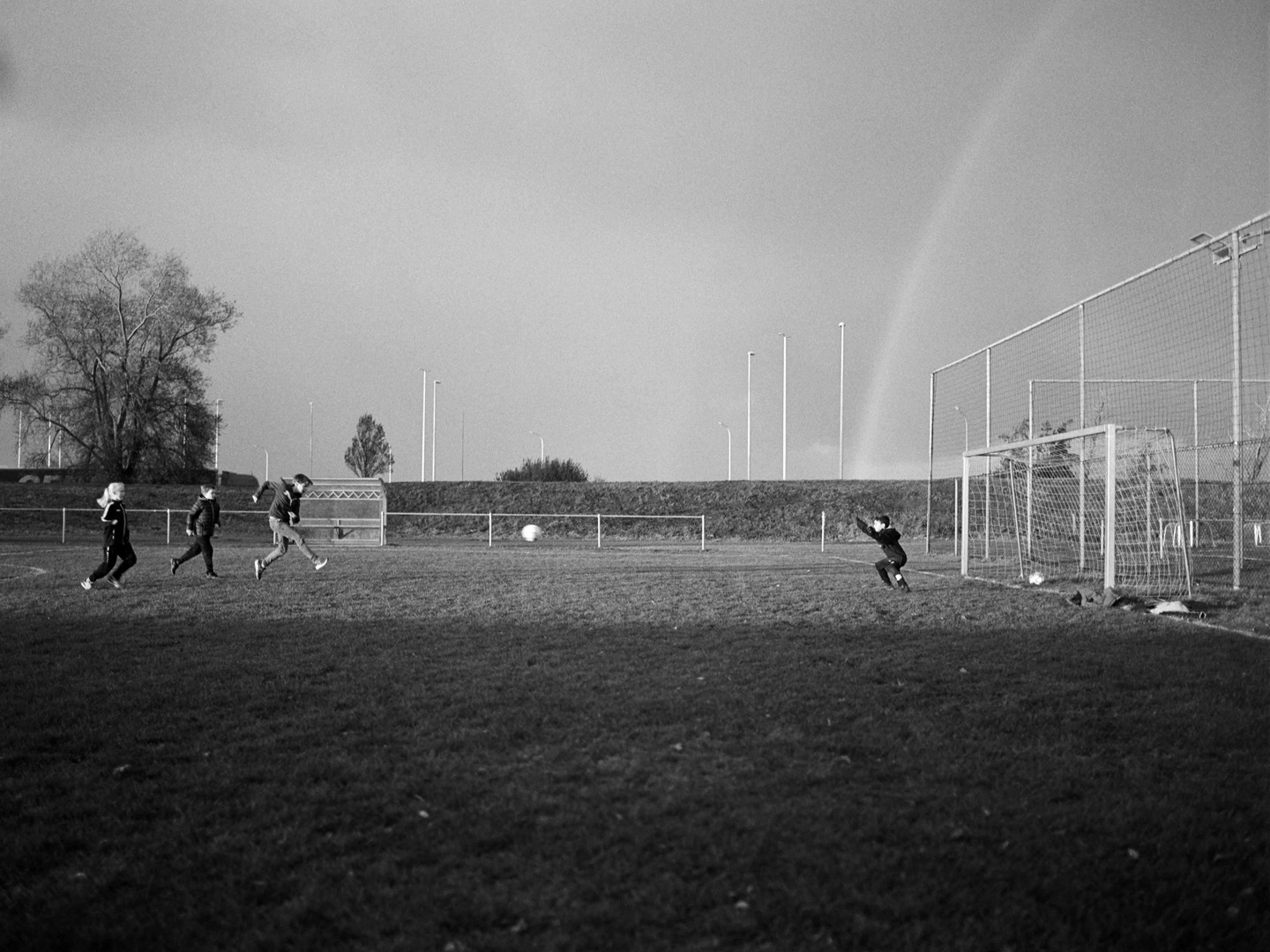 Children play football on a field with a rainbow in the background.