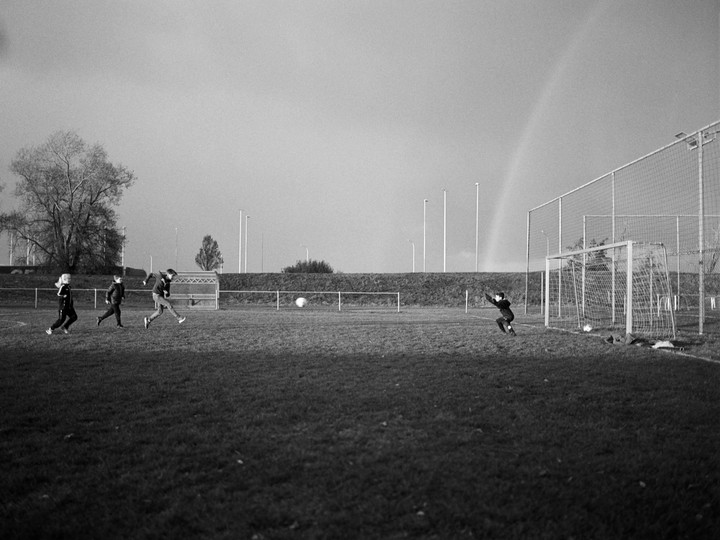 Children play football on a field with a rainbow in the background.