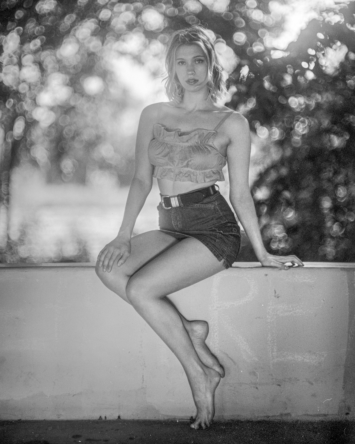 A woman with bare feet sits on a ledge with trees in the background.