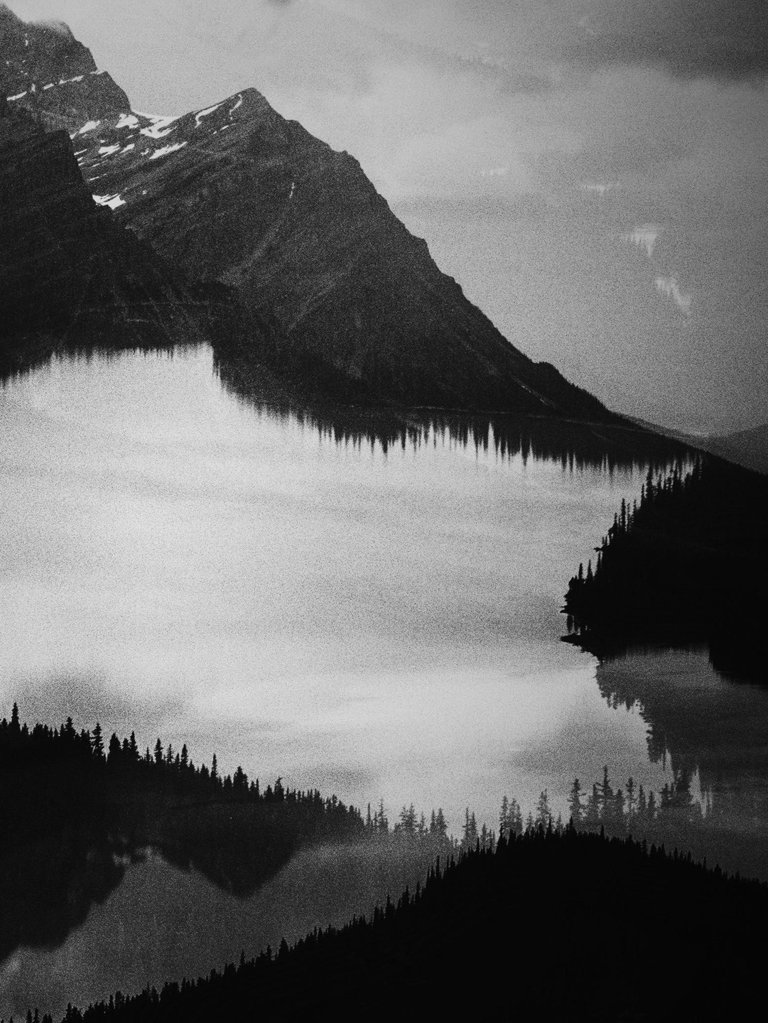 A double exposure shows a mountain reflected in a lake with a forest in the foreground.