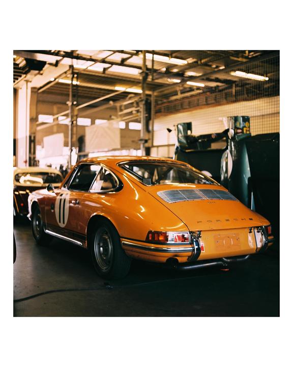 An orange vintage sports car with the number 11 on its side is parked in a garage.