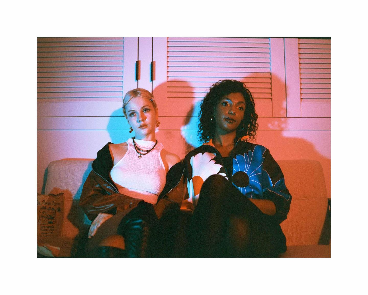 Two women sit on a couch in a room with red and blue lighting.