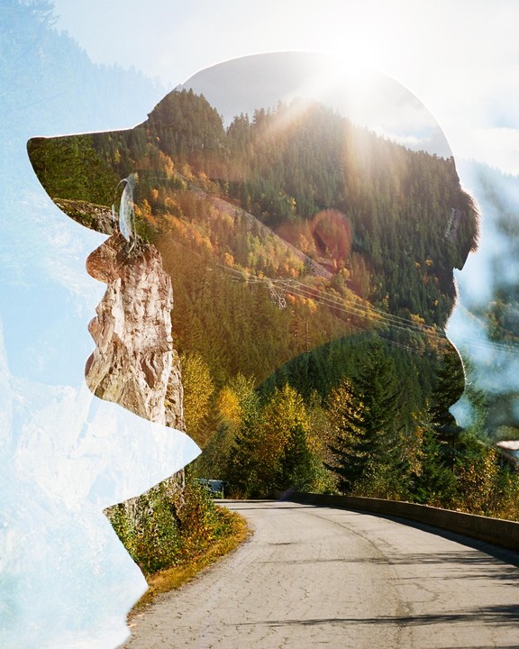 A double exposure shows a man's profile filled with a mountain landscape and a winding road.