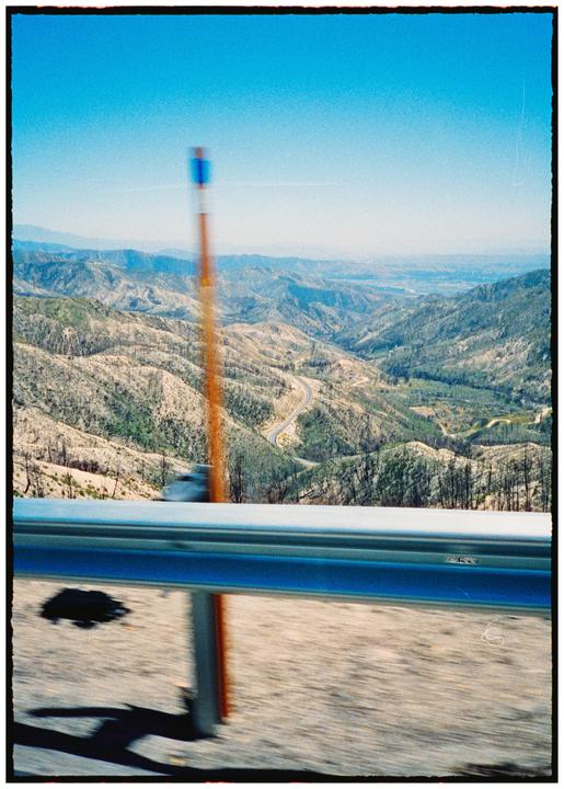 A winding road cuts through a mountainous landscape with a guardrail in the foreground.