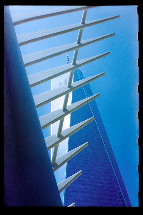A blue skyscraper is visible through a white architectural structure against a clear blue sky.